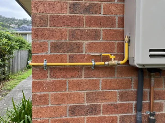 Yellow gas pipe and fittings on a brick exterior wall beside a home appliance in Allambie Heights