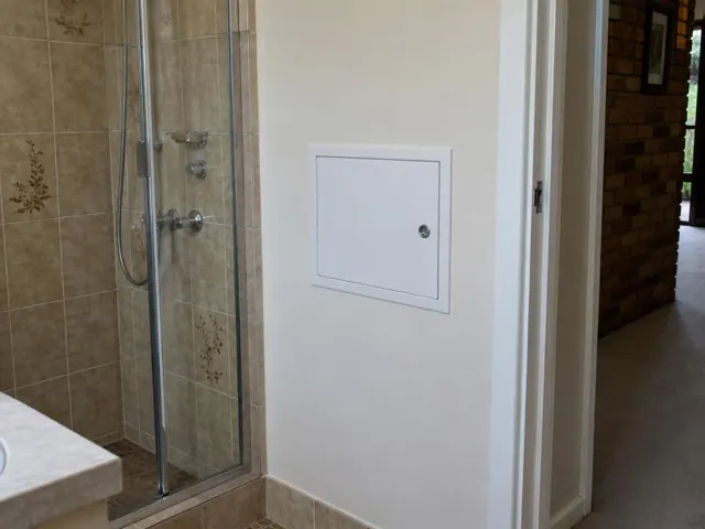 Small white access panel on a bathroom wall beside a shower and tiled floor in Frenchs Forest